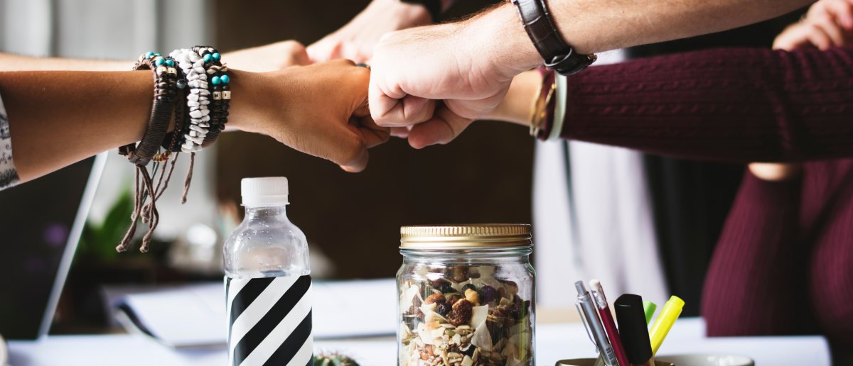 Several people fist bumping over a busy workspace